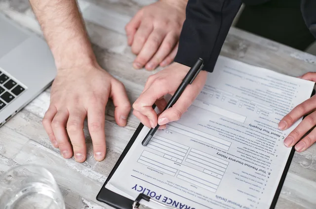 Close-up image of two people signing an insurance policy document on a wooden desk. Betriebshaftpflicht und Berufshaftpflicht: Welche Nachweise Auftraggeber verlangen können