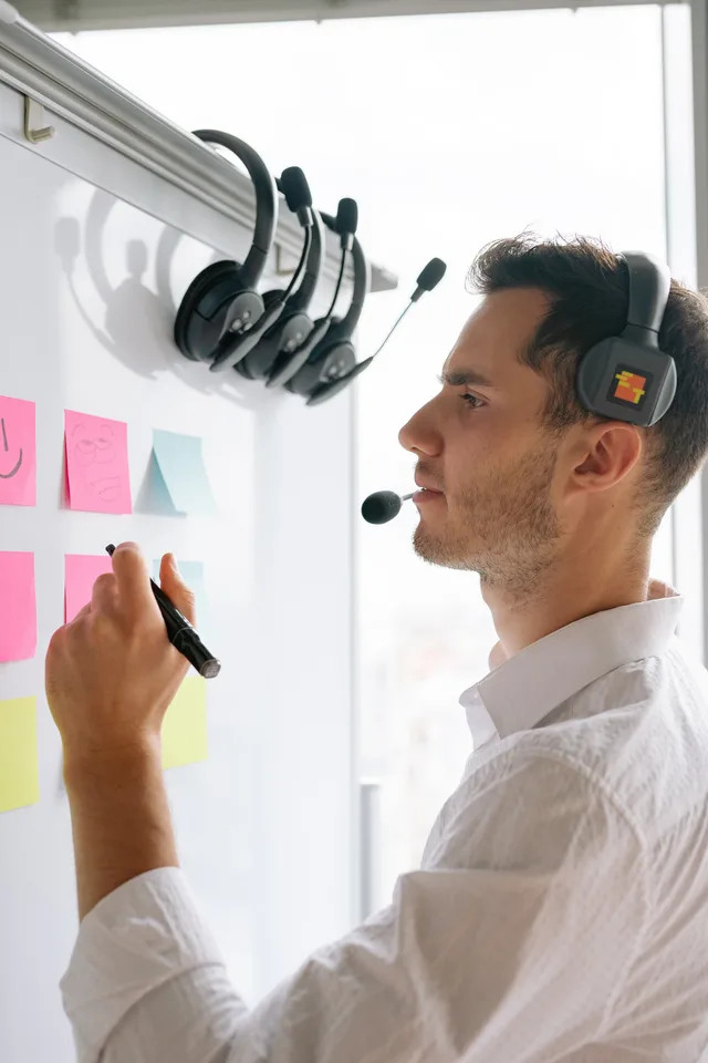 Two colleagues in formal attire discussing strategies on a whiteboard in a modern office space. Dienstleister finden: Bedarf klären, Angebote einholen, Auftrag vergeben