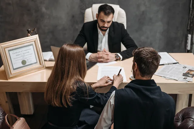 A lawyer discusses legal documents with clients in an office setting. Dienstleistungsverträge gestalten: Pflichten, Haftung und Kündigung in Österreich