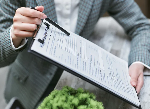Close-up of a businessperson holding a clipboard with an insurance document, emphasizing details. Nachweise prüfen: Gewerbe, Versicherung und Qualifikationen kontrollieren